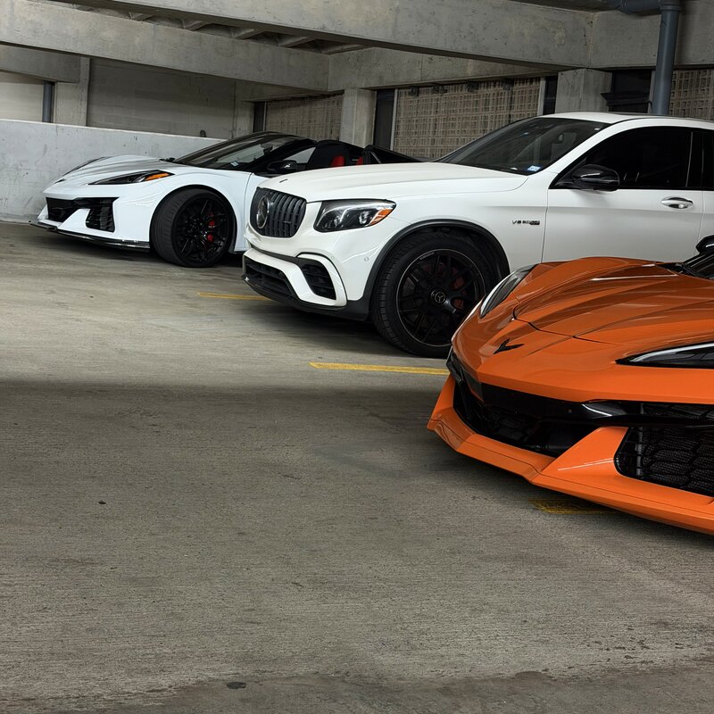 Full fleet lineup with white Corvette Z06, white Mercedes-AMG GLC 63 S, and orange Corvette Z06 in a garage