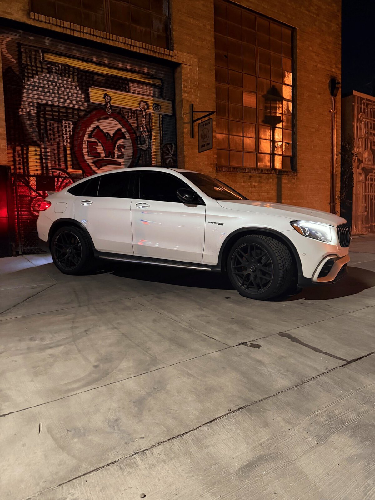 Mercedes-AMG GLC 63 S side profile beside a mural in a downtown alley at night